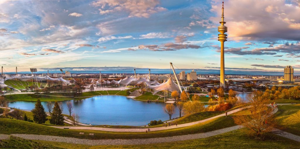 A captivating panoramic view of Munich's Olympic Park during sunset, showcasing the lake and iconic tower.